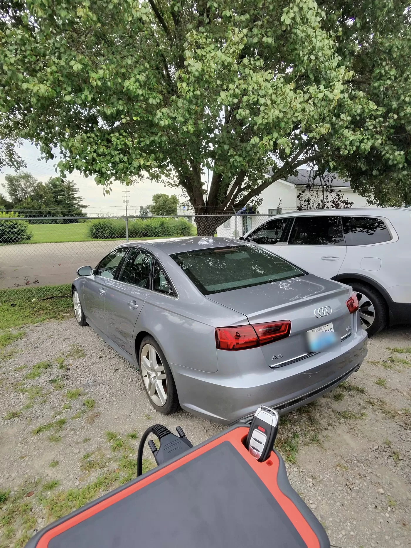 A silver Audi A6 parked on gravel with a key programming tablet and a new Audi key in the foreground.