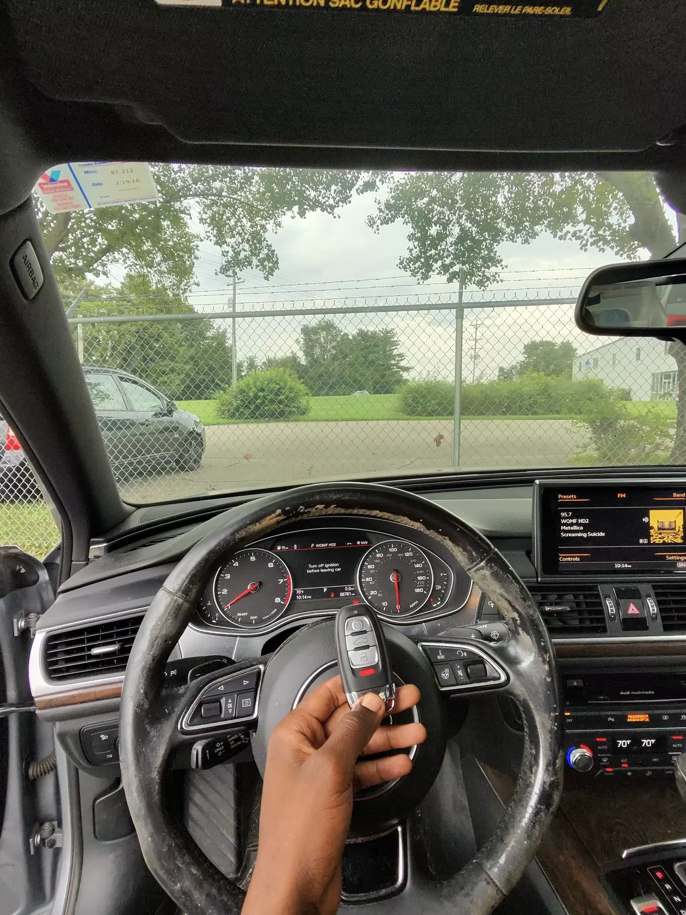 Inside an Audi A6, a hand holds a freshly programmed Audi smart key in front of the instrument cluster.