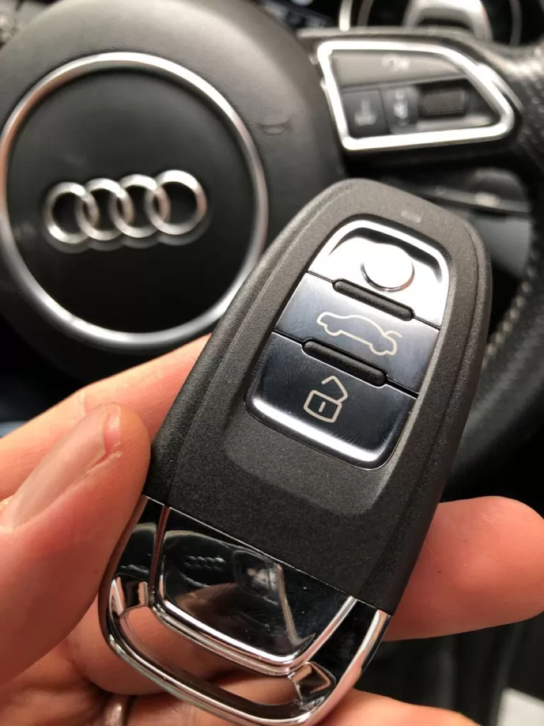 A replacement Audi proximity smart key held in front of an Audi steering wheel.