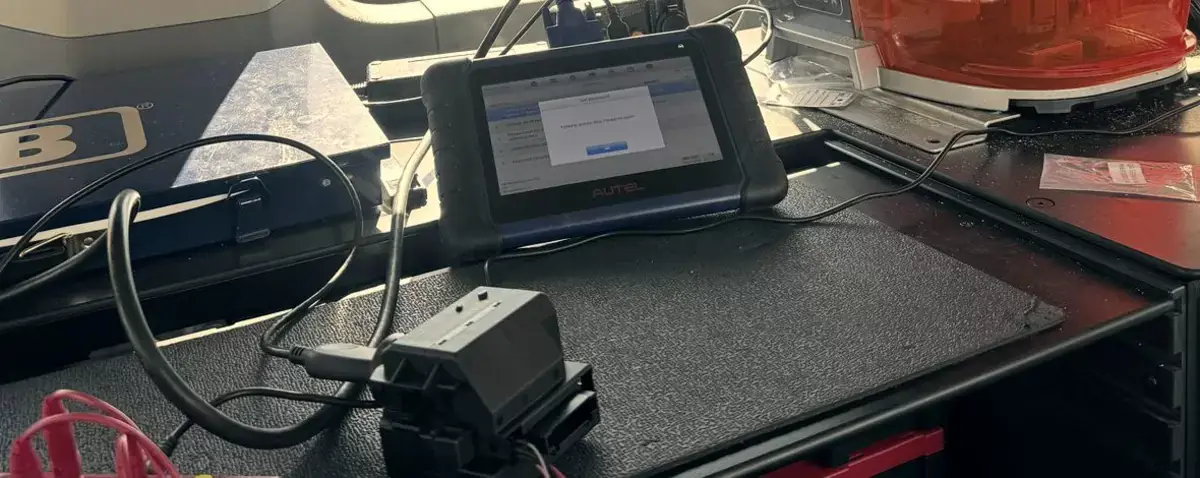 A diagnostic tablet on the bench connected to an OBD lead, with a breakout connector and programming cables laid out beside it.