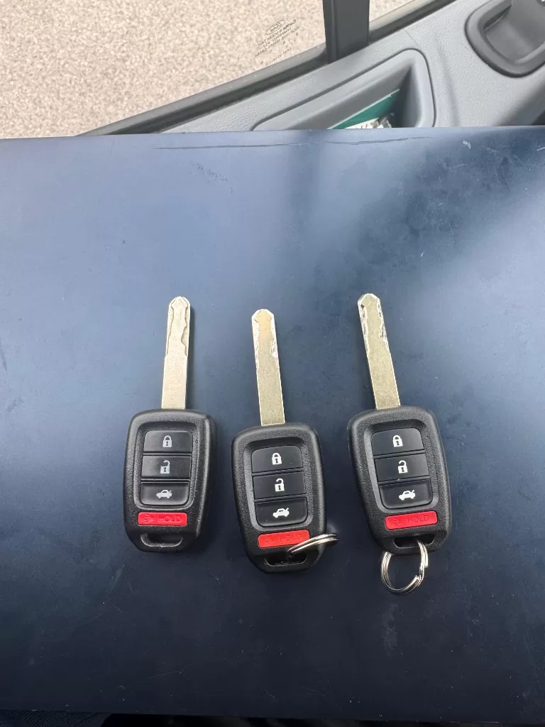 Three cut Honda remote head keys laid side by side on a dark work surface, blades freshly milled.
