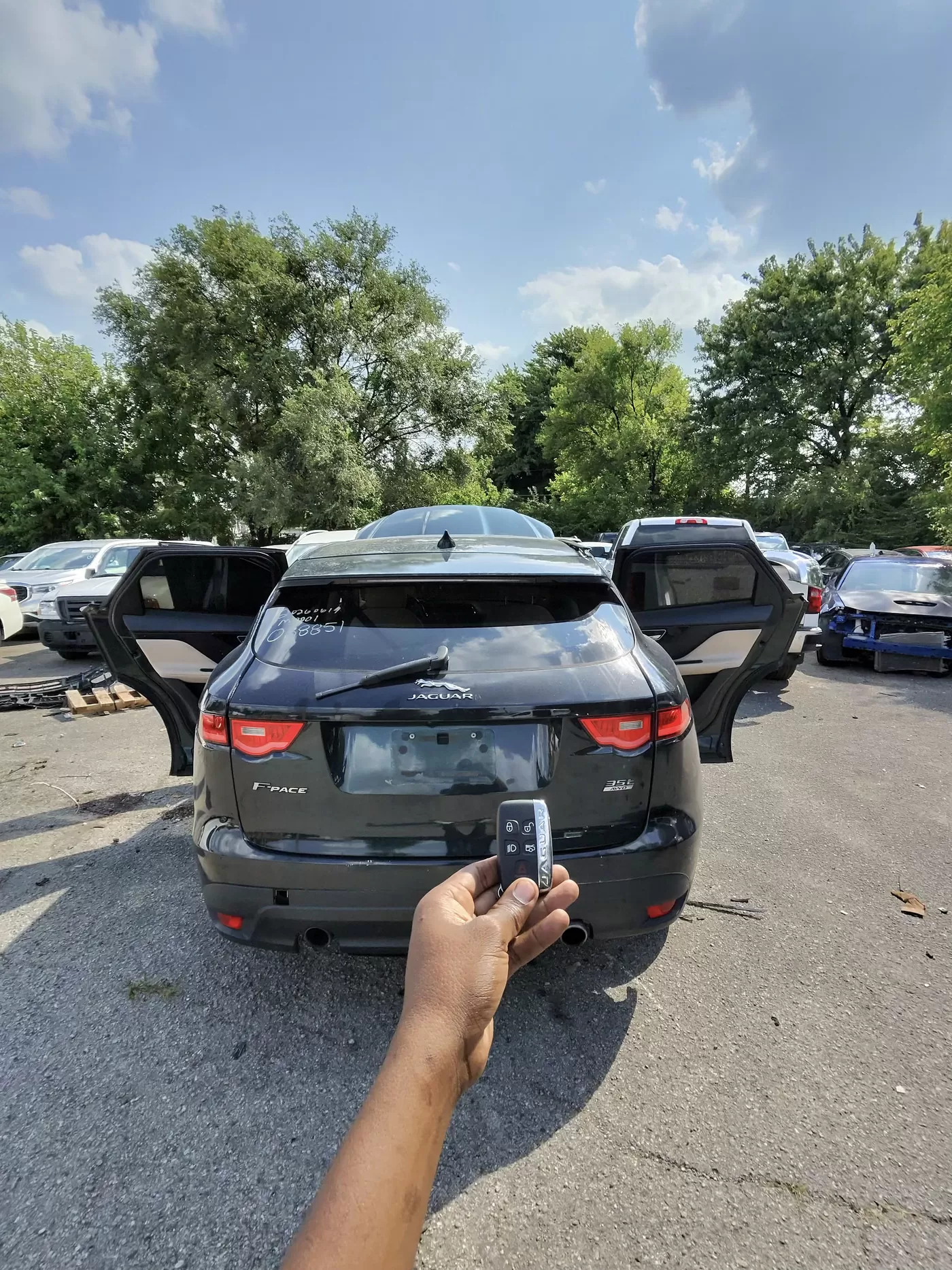 A newly programmed Jaguar key held up in front of a black Jaguar F-Pace with its doors open.