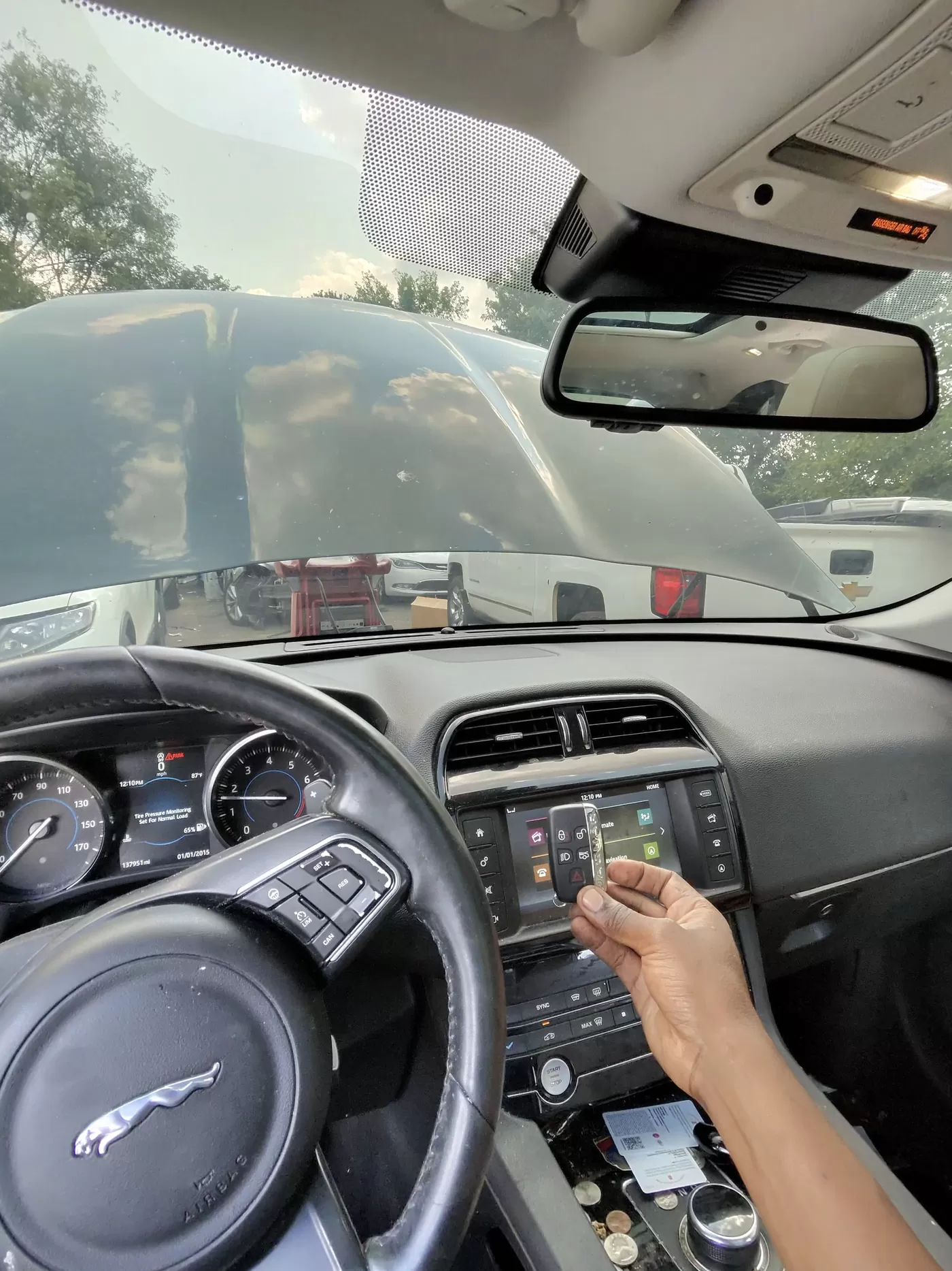 Inside a Jaguar, a hand holds a key fob next to the center touchscreen during programming.