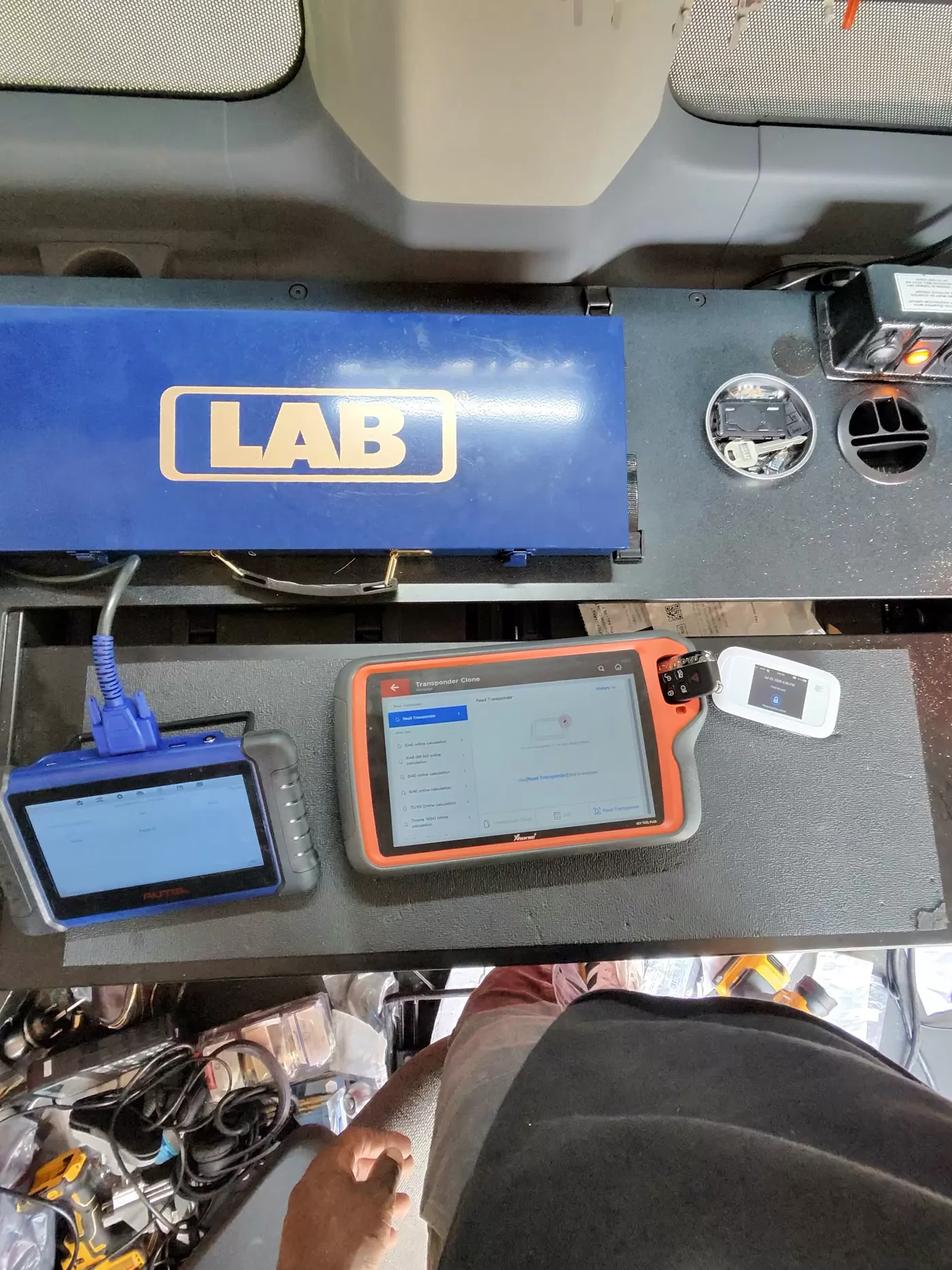 Two key programming tablets on the van bench, one showing a transponder cloning screen mid-read, with a remote key beside it.