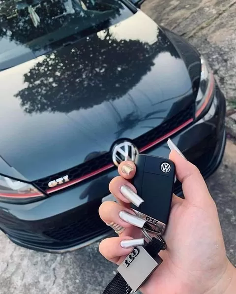 A Volkswagen flip key fob held in front of the grille of a black Golf GTI.
