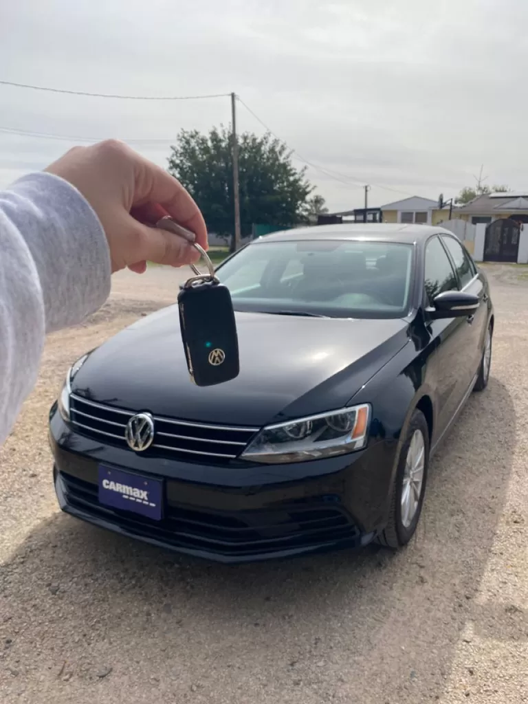 A newly cut Volkswagen key held up in front of a black Volkswagen Jetta.